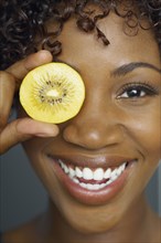 African woman holding fruit slice in front of eye