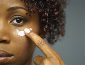 Close up of African woman applying cream under eye