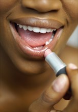 Close up of African woman applying lipstick