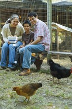 Multi-ethnic family holding bowl of eggs next to chickens