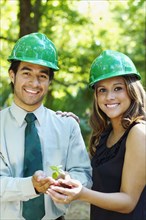 Hispanic business people with green hard hats holding tree sprout