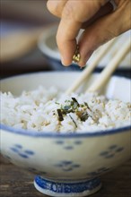 Hand putting seasoning on bowl of rice with chopsticks