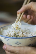 Person eating bowl of rice with chopsticks