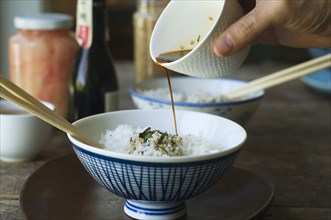 Person pouring sauce over bowl of rice