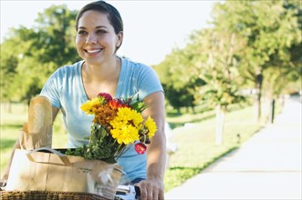 Mixed race woman riding bicycle with flowers in basket