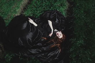 Caucasian woman wearing black dress sleeping on grass