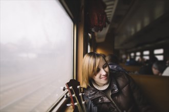 Smiling Caucasian woman with guitar sitting near window on train