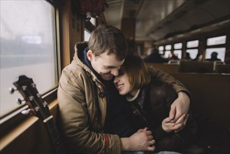 Smiling Caucasian couple with guitar hugging on train
