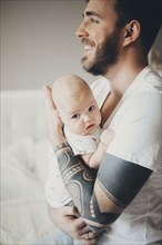 Caucasian father with tattoos on arms holding baby son