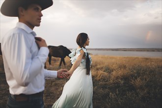 Caucasian woman holding hands with cowboy near river