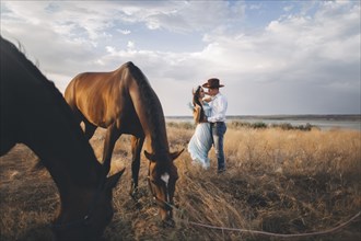 Horses grazing near Caucasian woman hugging cowboy