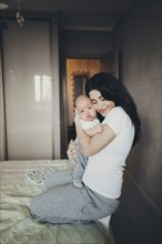 Caucasian mother kneeling on bed hugging baby son