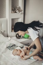 Caucasian mother changing diaper of baby son on bed