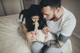 Caucasian mother and father on bed playing with baby son