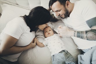 Caucasian mother and father holding hands with baby son on bed