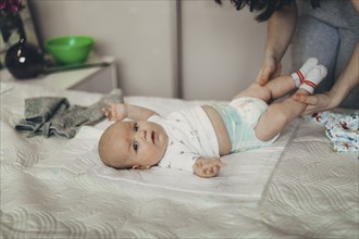 Caucasian mother changing diaper of baby son on bed