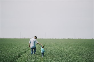 Caucasian father and son holding hands and walking in field