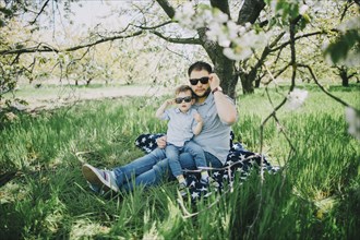 Caucasian father and son wearing sunglasses on blanket in grass