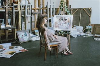 Caucasian artist sitting near painting on easel