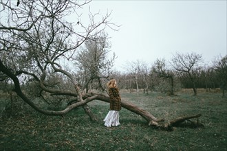 Caucasian woman wearing fur coat near fallen tree