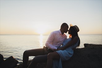 Caucasian couple rubbing noses near ocean at sunset
