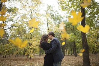 Autumn leaves falling near hugging Caucasian couple