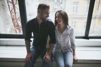 Caucasian couple sitting on window sill holding hands