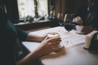 Hands of Caucasian couple drinking coffee and wine