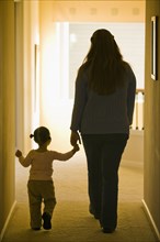 Hispanic mother and daughter walking in hallway