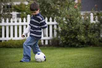 Mixed race boy playing soccer in backyard