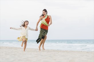 Hispanic mother and daughter running on beach