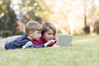 Caucasian boys using digital tablet on lawn