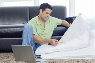 Hispanic man examining blueprints in living room