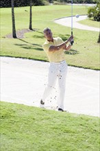 Caucasian man golfing from sand trap on golf course