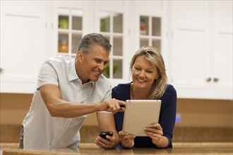 Caucasian couple using digital tablet and cell phone at kitchen counter