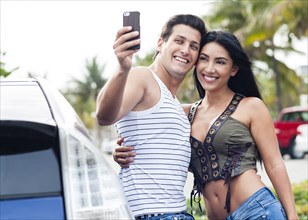 Hispanic couple taking cell phone selfie outdoors