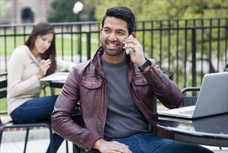 Indian man talking on cell phone at table outdoors