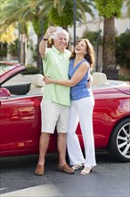 Older Caucasian couple taking cell phone photograph near convertible