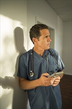 Hispanic doctor leaning on wall using cell phone