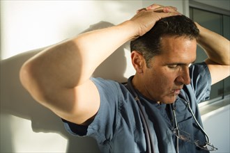 Stressed Hispanic doctor leaning on wall