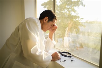 Stressed Hispanic doctor standing at window