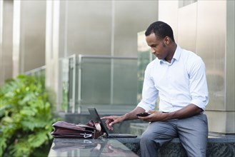 Black businessman using laptop outside building