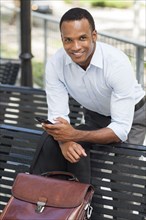 Black businessman using cell phone on park bench