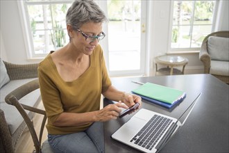 Woman using cell phone and laptop in living room