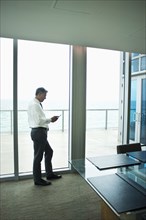 Caucasian businessman using cell phone at office window