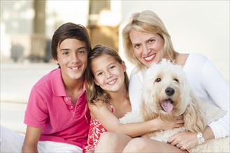 Smiling mother and children posing with dog outdoors