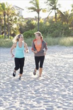 Caucasian mother and daughter jogging on beach