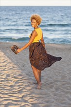 Black woman carrying sandals on beach