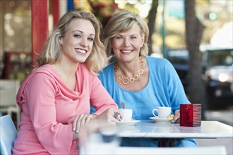 Caucasian mother and daughter drinking coffee at sidewalk cafe