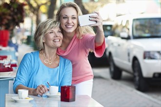 Caucasian mother and daughter taking selfie at sidewalk cafe